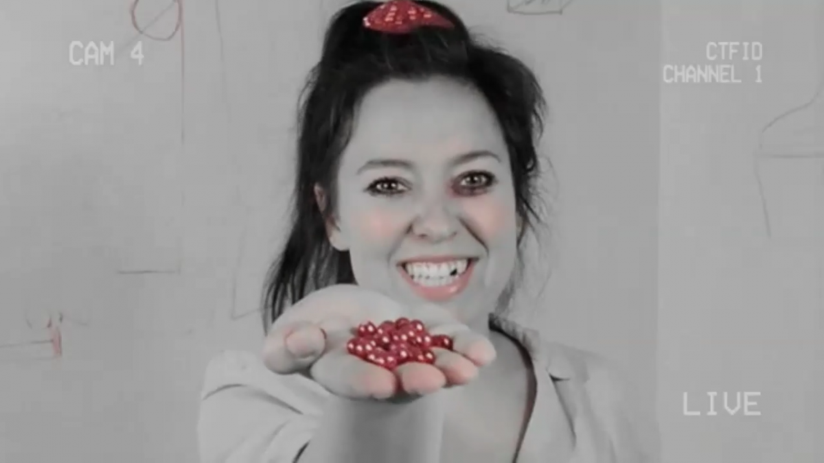 A woman with dark hair and grayed out complexion offers a handful of beads to the viewer while smiling.