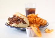 Steak and cheese sub, curly fries, ketchup and a glass of soda with ice.