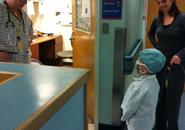A young boy shown dressed as a doctor is in a hospital smiling up at nurses