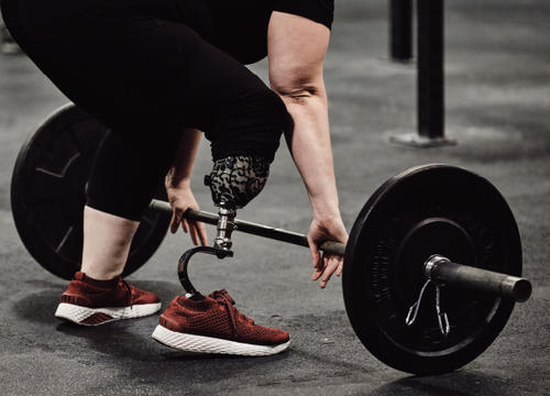 Melissa DeChellis reaches for a barbell, showing her prosthetic leg