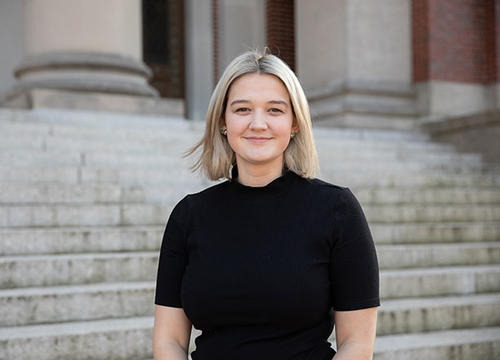 Emma Powell stands on the steps of Dinand Library