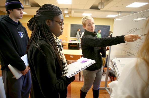professor pointing to a chalkboard as a group of students look on