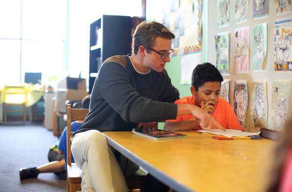 a Holy Cross student volunteer helps a young student with an activity
