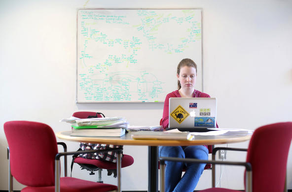 student working on a laptop with whiteboard behind her