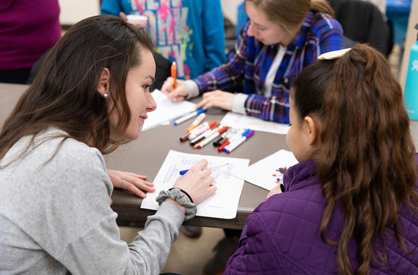 a Holy Cross student volunteer helps a young student with an activity