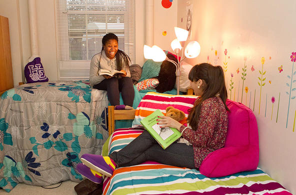 two students sitting on their beds holding books and laughing