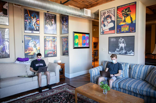 two students sitting on separate couches and working on laptops in their apartment room with posters decorating the walls 