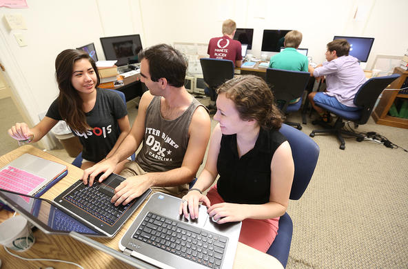 three students sitting at two laptop computers at the same desk