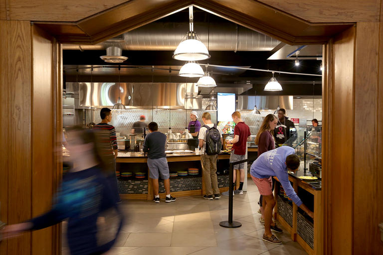 Students inside the Kimball Dining Hall servery waiting at various stations for food.