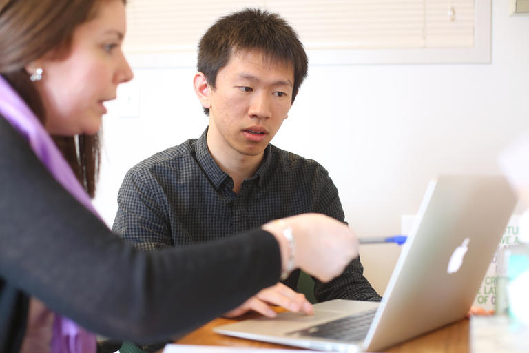 Two people discussing what they are looking at on a laptop.