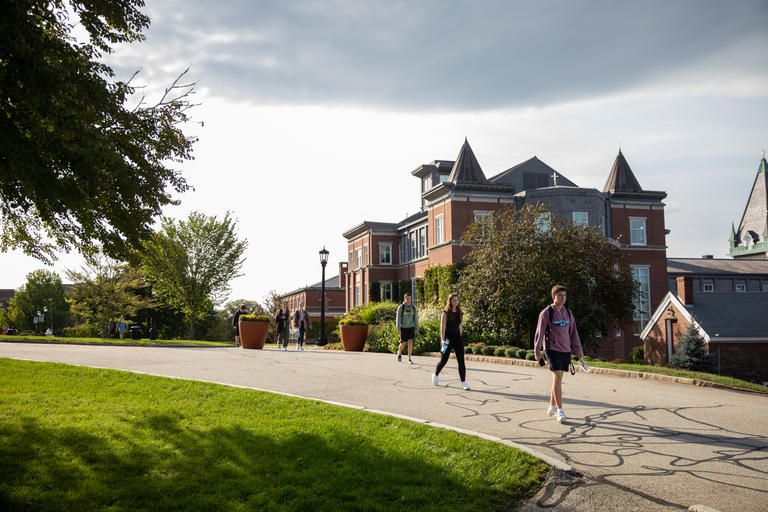 A late summer day with a few students walking down a campus driveway near campus housing.