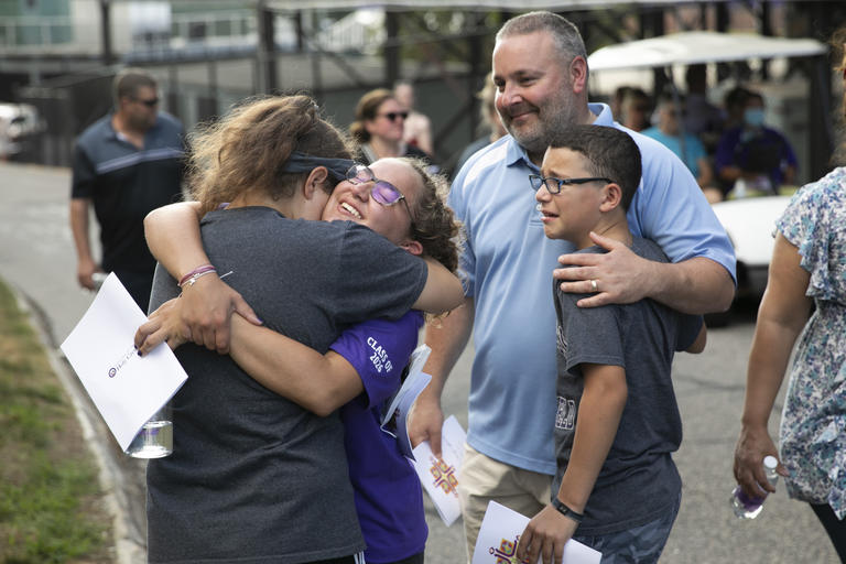 Student hugging her family member while other family members embrace behind her. It is an emotional moment celebrating some milestone.