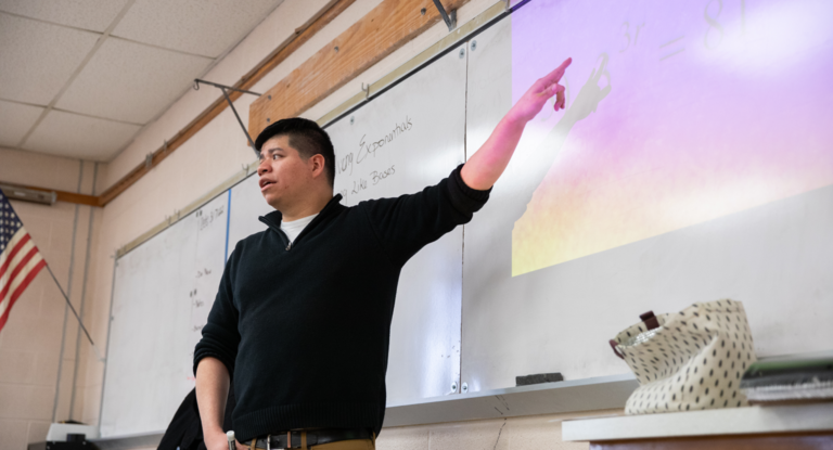 Teacher standing in front of a whiteboard pointing while teaching.
