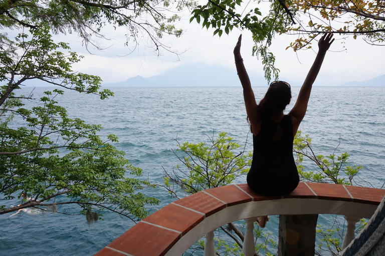 student sitting on a fence overlooking the water, with arms outstretched