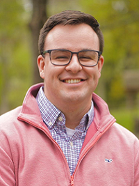 Patrick Rogers Associate Director Student involvement man with salmon color pullover and glasses blurred green background