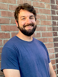 close up picture of man with dark hair and beard with a blue short sleeve shirt