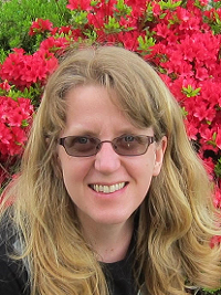 woman with sunglasses on long light hair with red flowers behind her