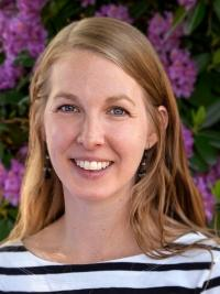 headshot of woman with light colored hair and a blue and white stripped shirt on pink flowers behind her