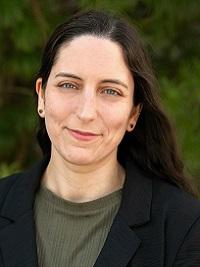 headshot of a woman with long black hair smiling with a dark blazer and olive green top