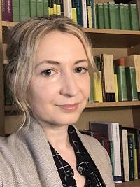 close up picture of a women with blond hair smiling at the camera with a bookshelf behind her