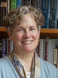 close up of a faculty member with a bookcase behind her, she is smiling at the camera