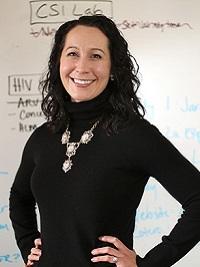 faculty member standing in front of a white board with writing smiling at the camera