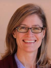 close up picture of a woman with blond hair, wearing glasses smiling at the camera