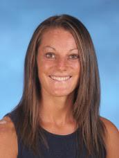headshot of a woman wearing a sleeveless dark dress, long brown hair, blue background smiling at the camera 