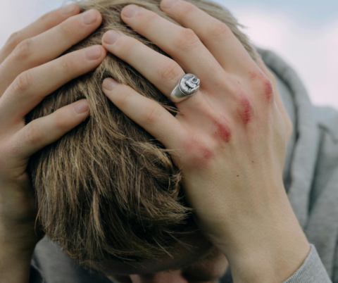 Trauma a young man holding his hands across his head